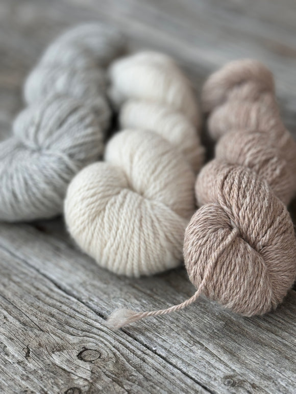 3skeins of yarn lay on a table. From
left to right they are light grey, natural white and honeycomb 