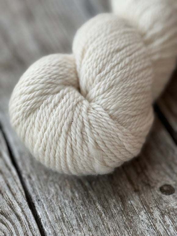 A natural coloured white skein is laying on a wooden table 